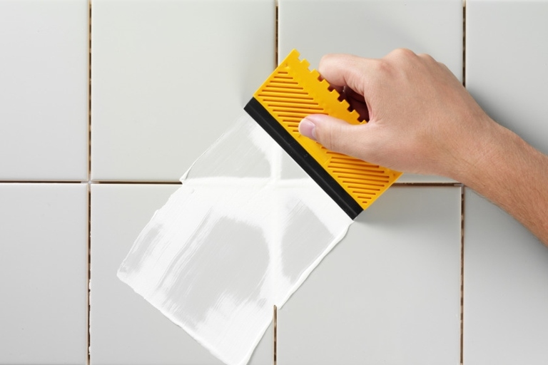 To remove soft grout from a tub's surface, use a putty knife or old toothbrush to scrape it away.
